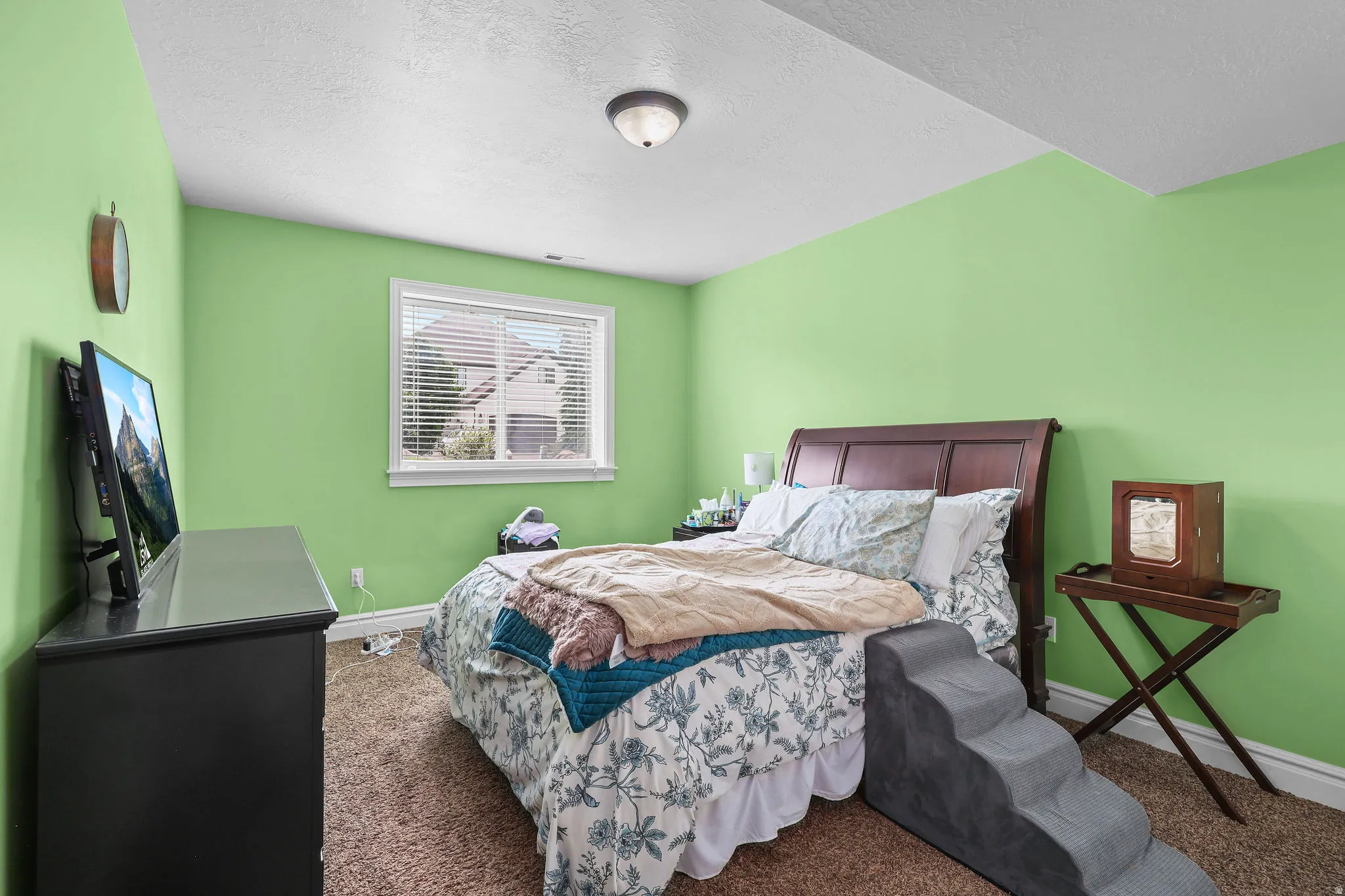 Window with blinds, wood-finish headboard, built-in ceiling light fixture, and brown carpet flooring
