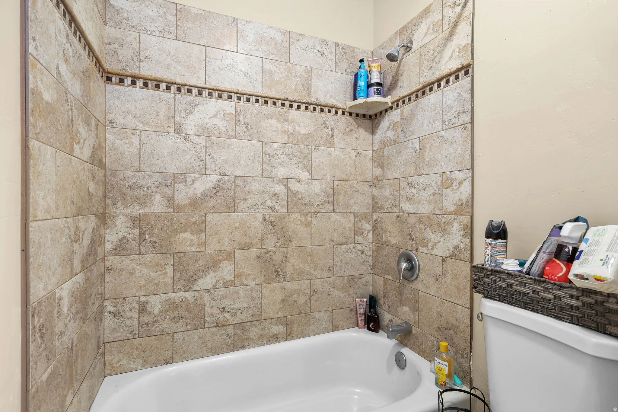 Bathtub and shower combination featuring neutral-toned subway tile surround, decorative mosaic accent tile, and a corner shower shelf