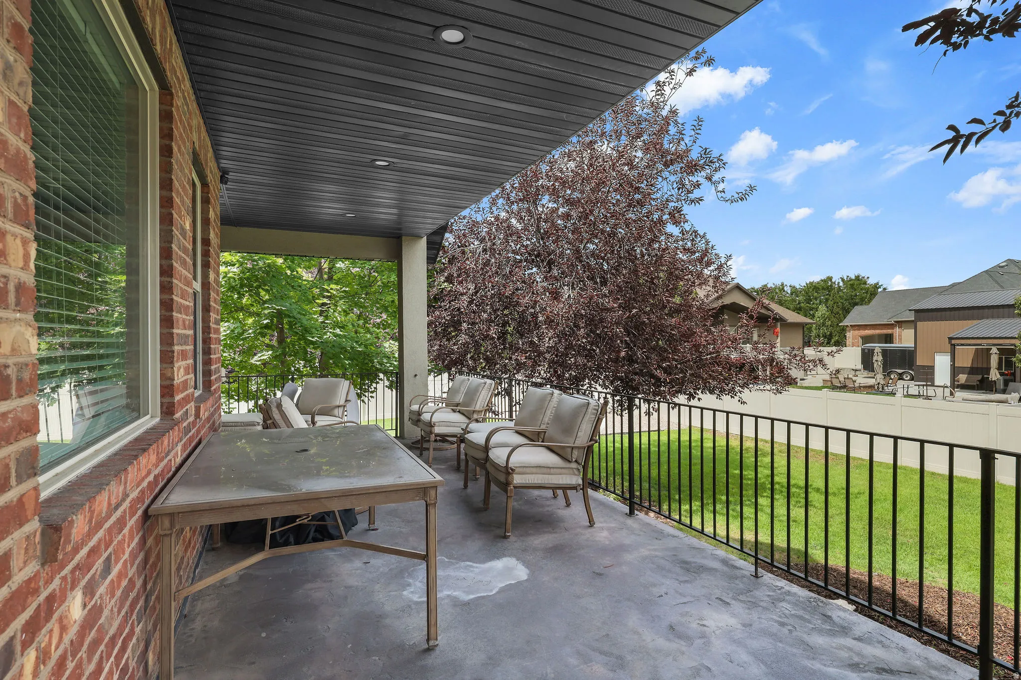Covered patio featuring a stamped concrete surface, recessed lighting, a brick exterior wall, a black metal railing, and a mature tree