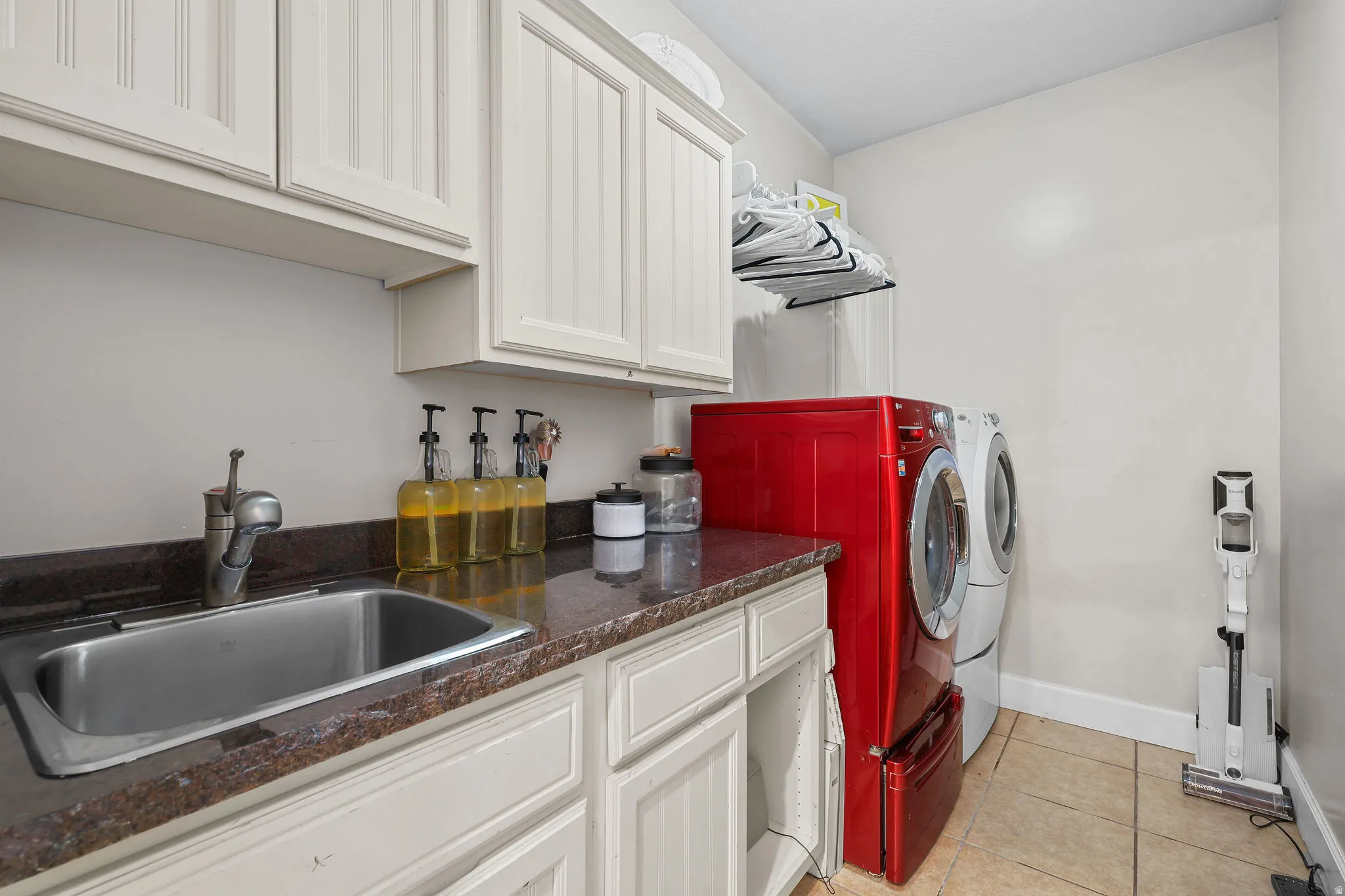 Utility room featuring white cabinetry, a stainless steel sink, a dark countertop, and tiled flooring