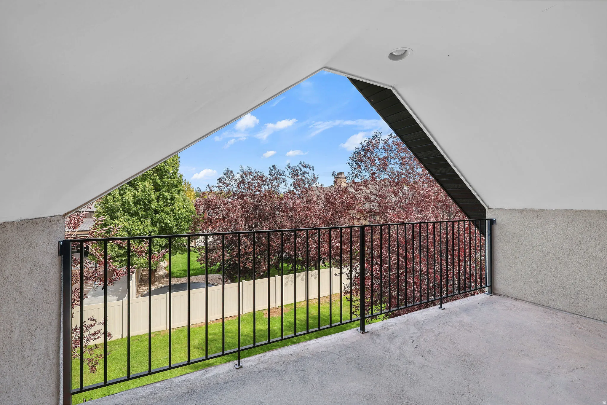 Private balcony with textured concrete flooring, black metal railing, and recessed lighting