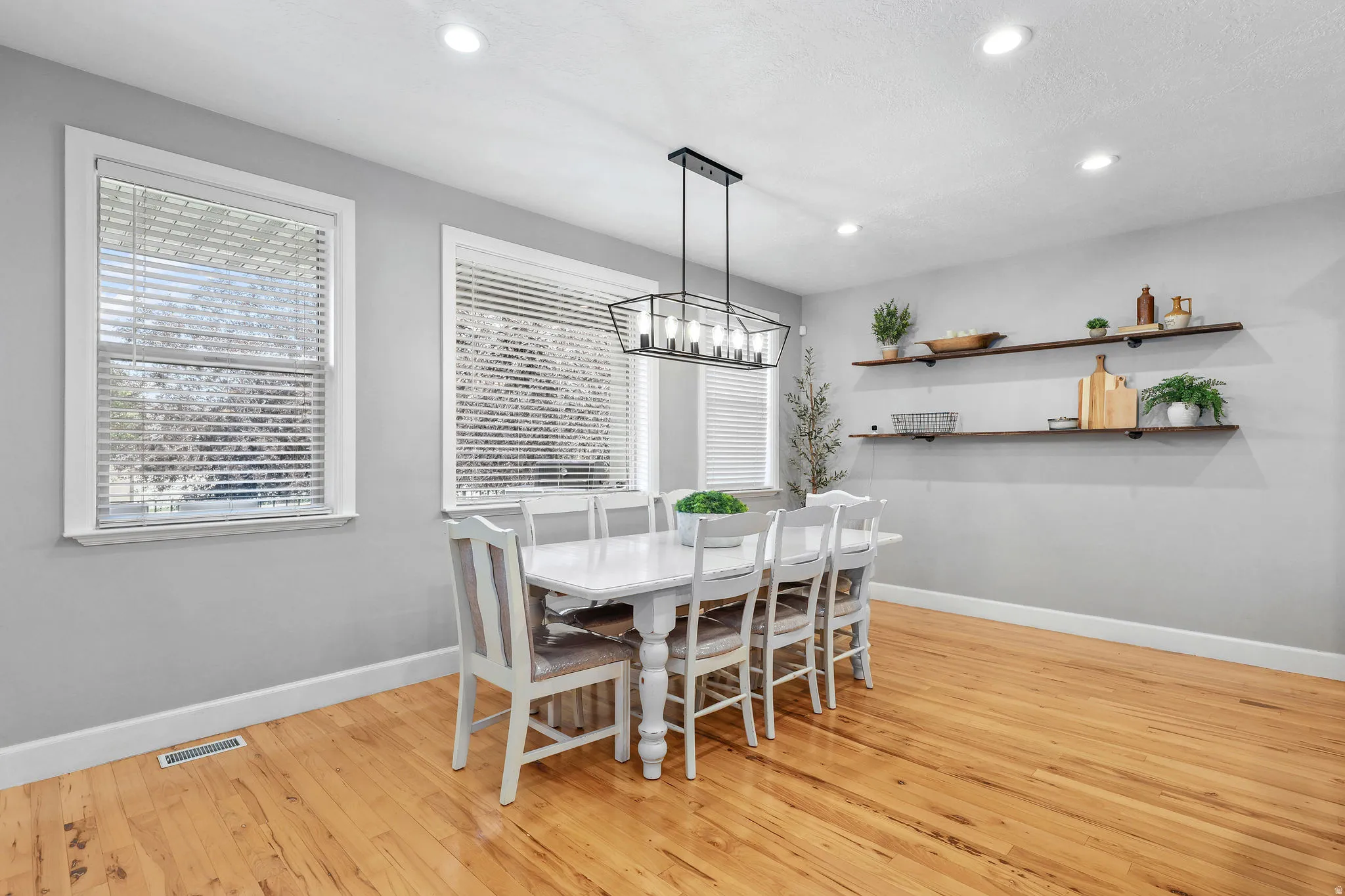Hardwood flooring, recessed lighting, two windows with white trim, open shelving, and a linear chandelier