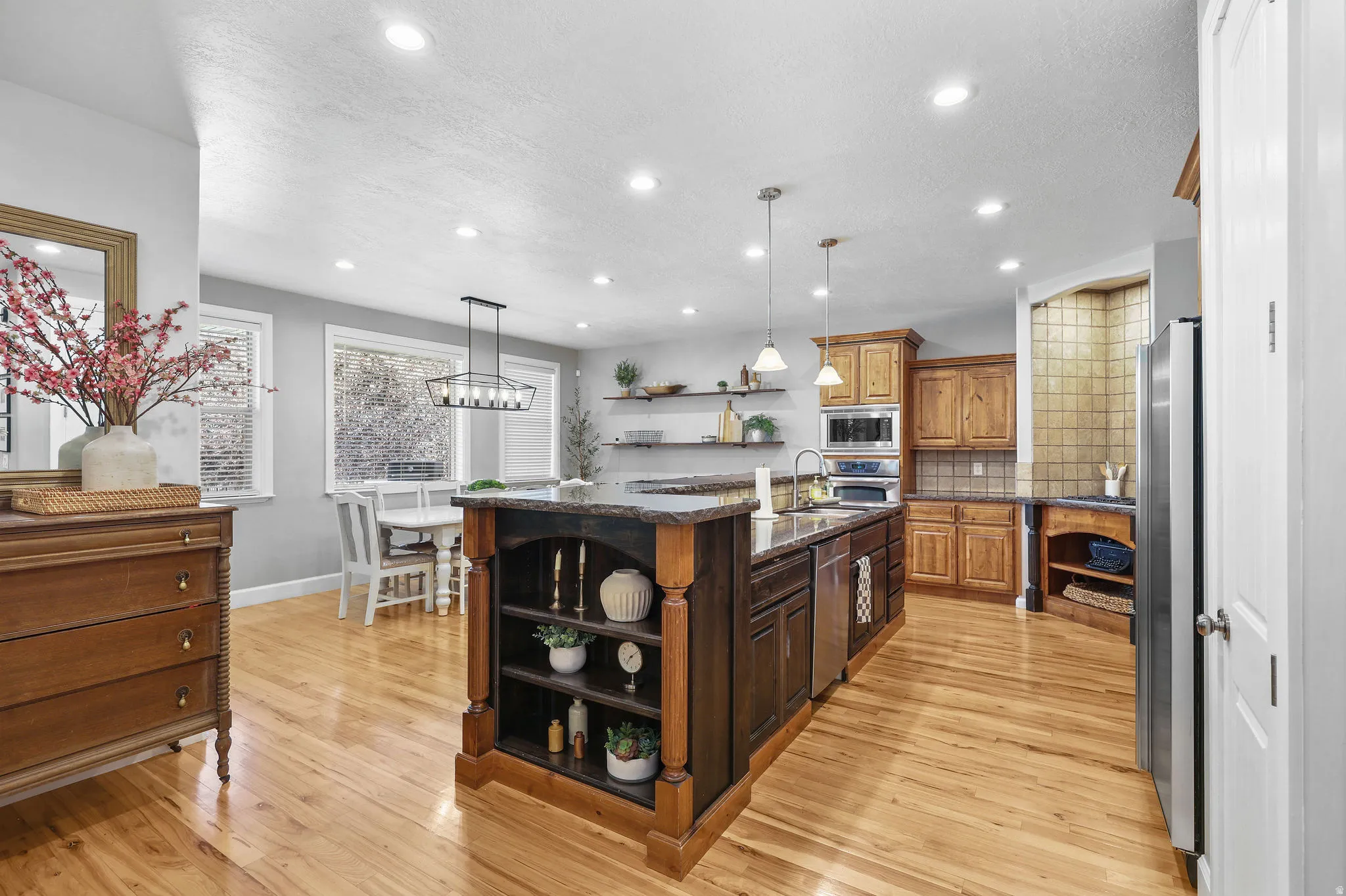 Hardwood flooring, recessed lighting, expansive kitchen island with integrated shelving, stainless steel appliances, and wood cabinetry