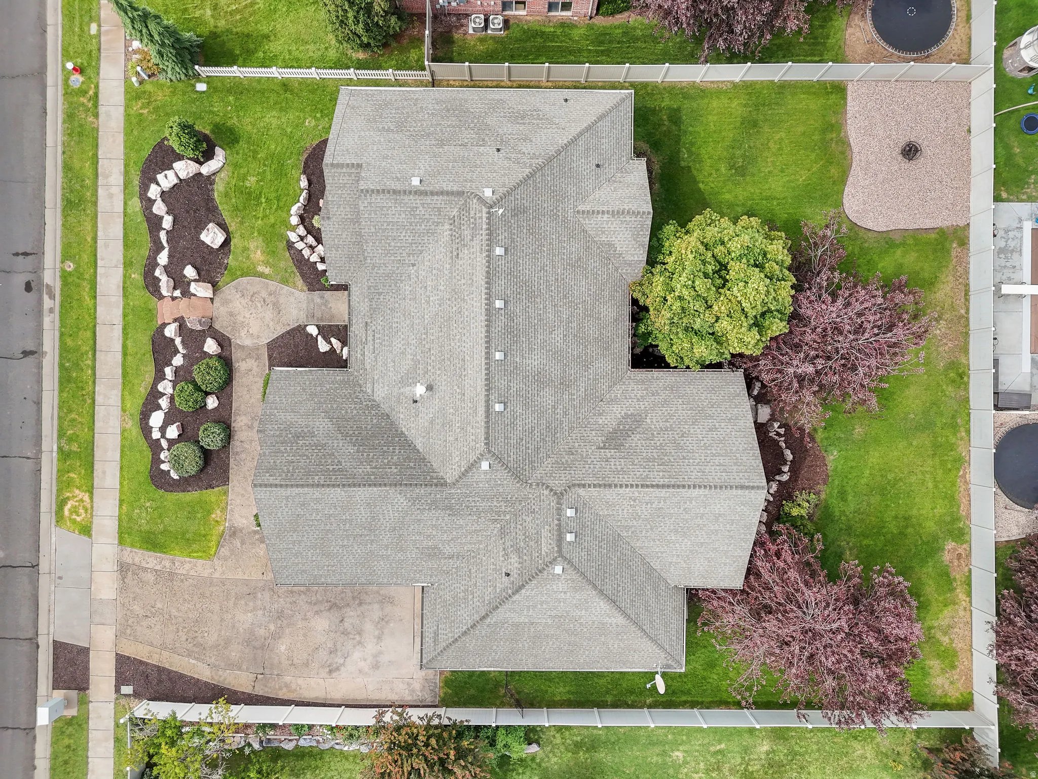 Pitched roofline, expansive green lawn, mature trees, landscaped beds with decorative rocks, and a paved driveway