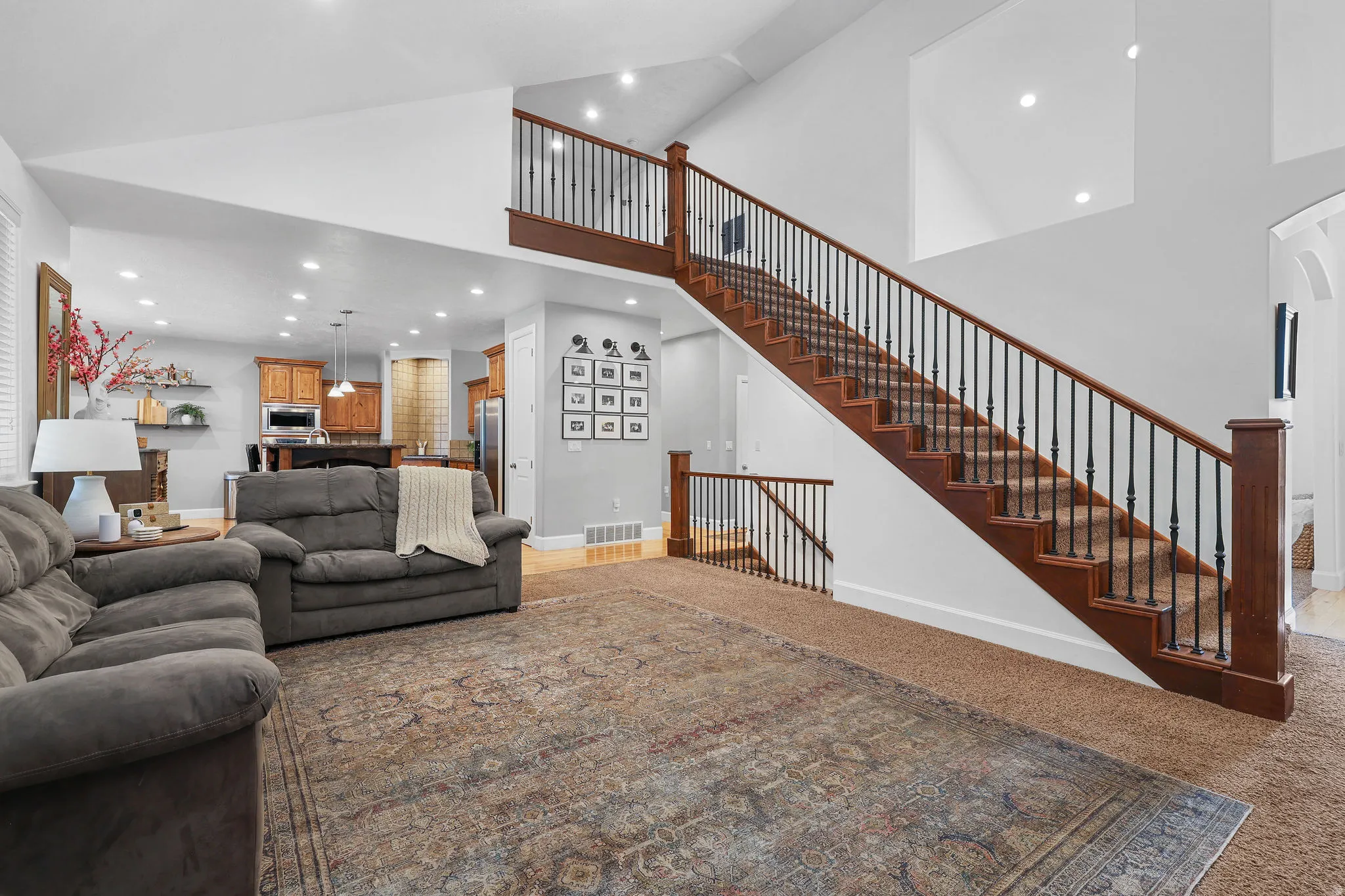 Two-story ceiling, recessed lighting, wood staircase with iron balusters, wood-finish flooring, built-in kitchen cabinetry