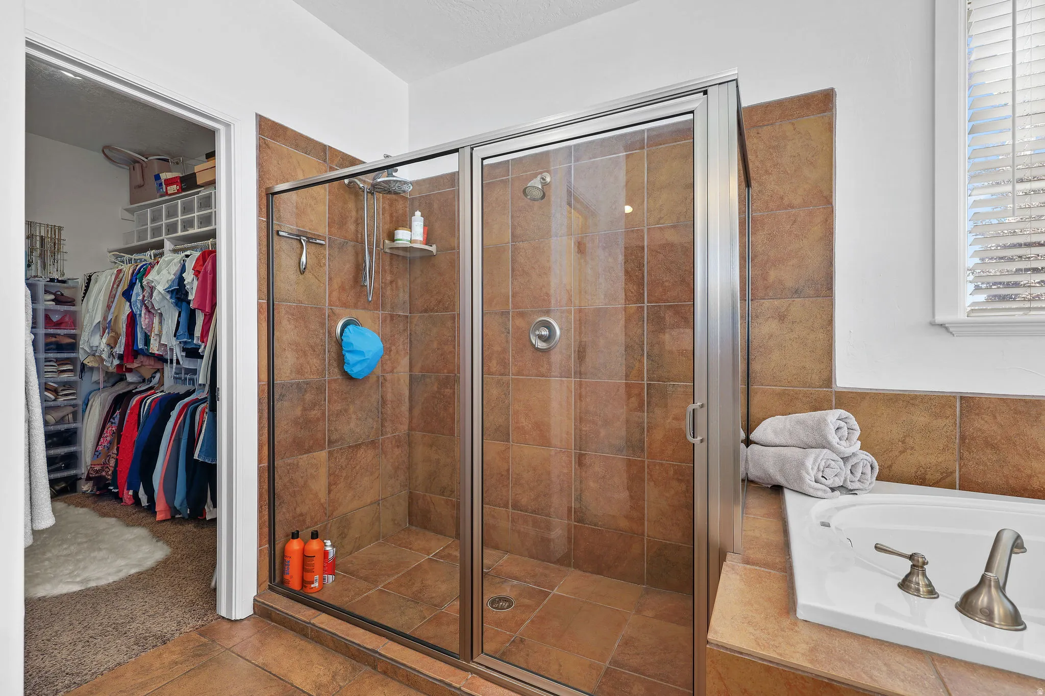 Tiled walk-in shower with a glass enclosure, an integrated bathtub, and a separate closet with built-in shelving