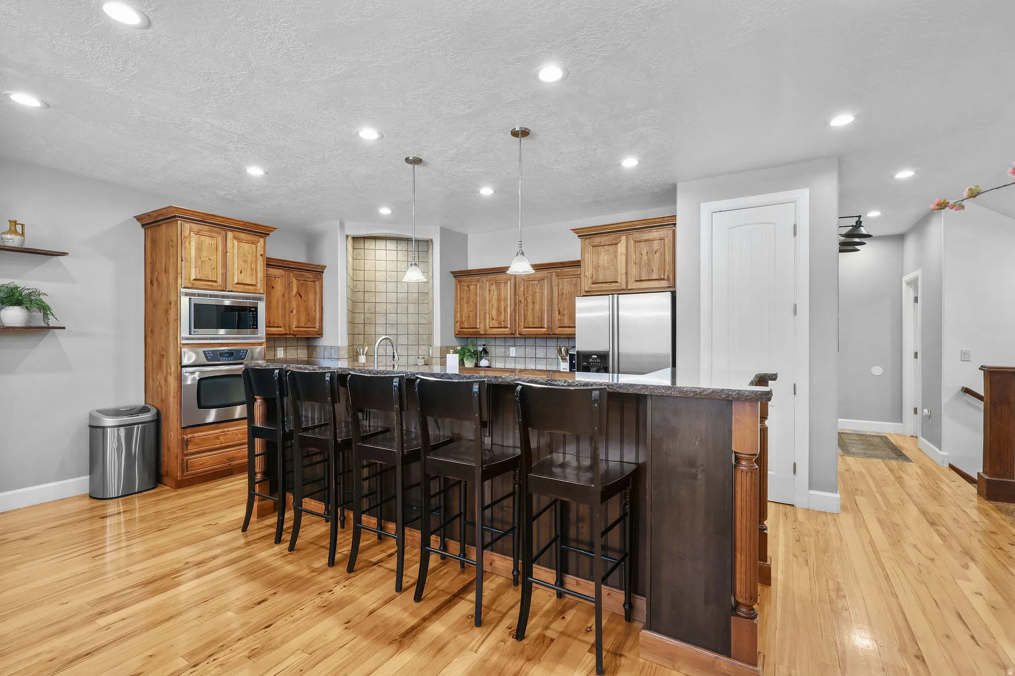 Wood-finish flooring, recessed lighting, wood cabinetry, stainless steel appliances, and a kitchen island with pendant lighting