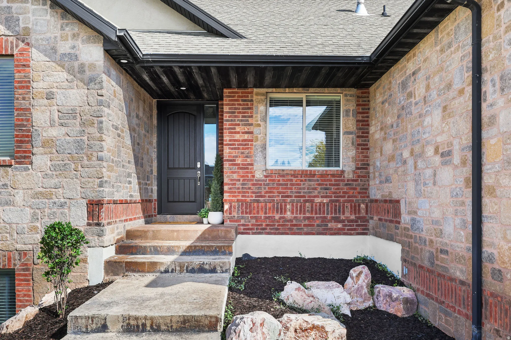 Stone and brick facade with a dark entry door, concrete steps, and integrated landscaping