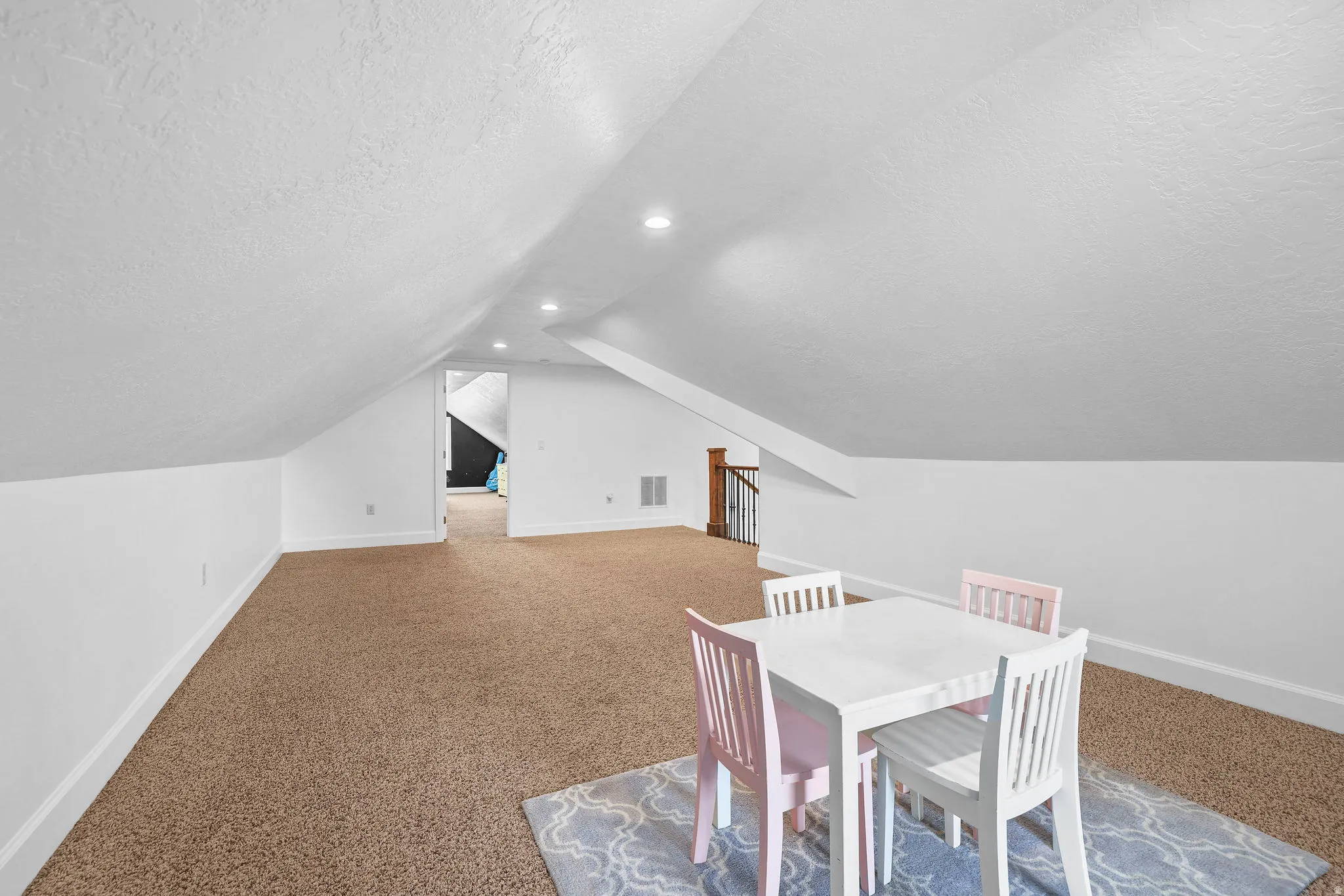 Carpeted floor, white painted walls, vaulted ceiling, recessed lighting, and a wood-finish staircase railing