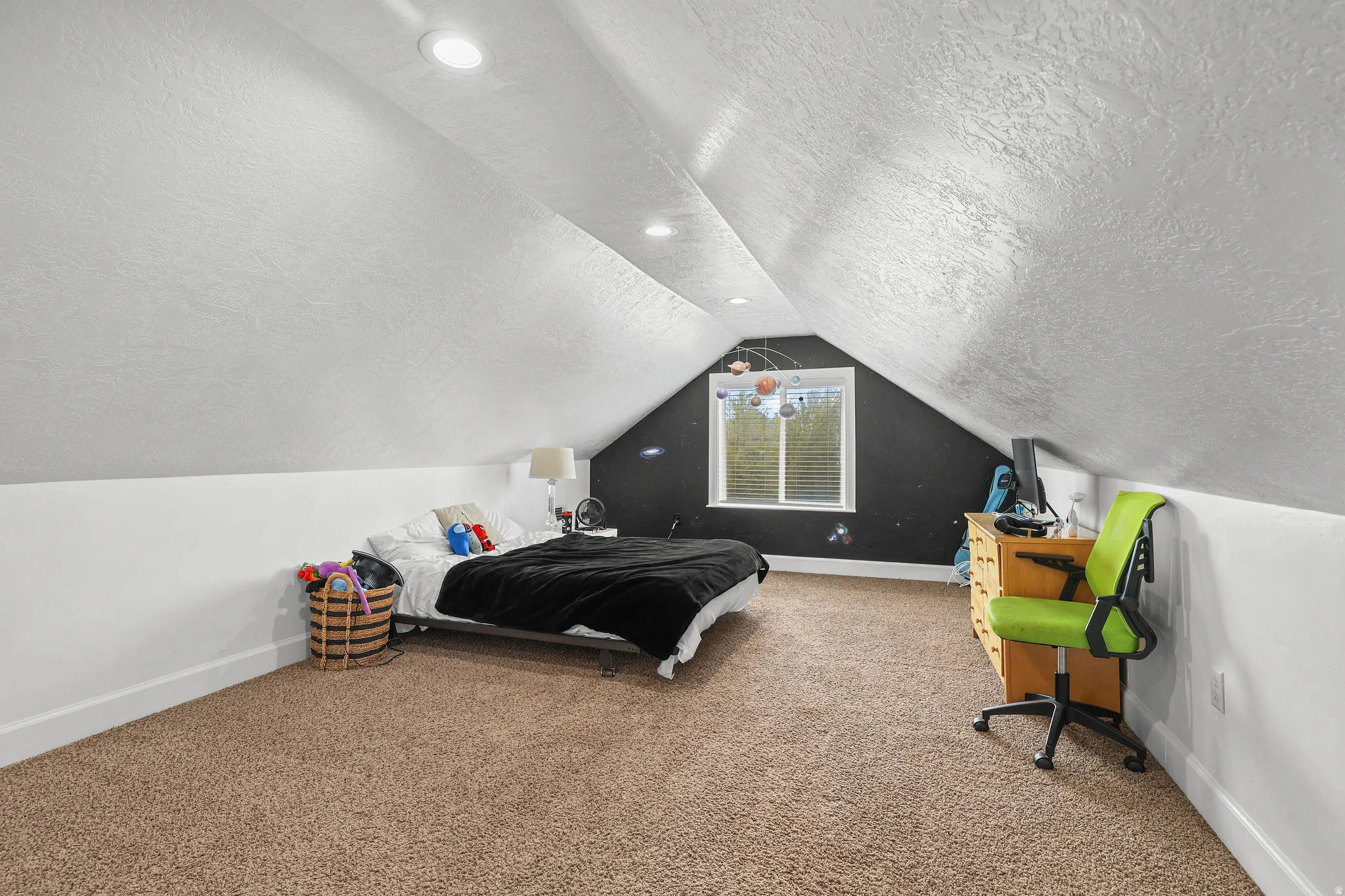 Recessed lighting illuminates a spacious room featuring a sloped ceiling and a window with blinds