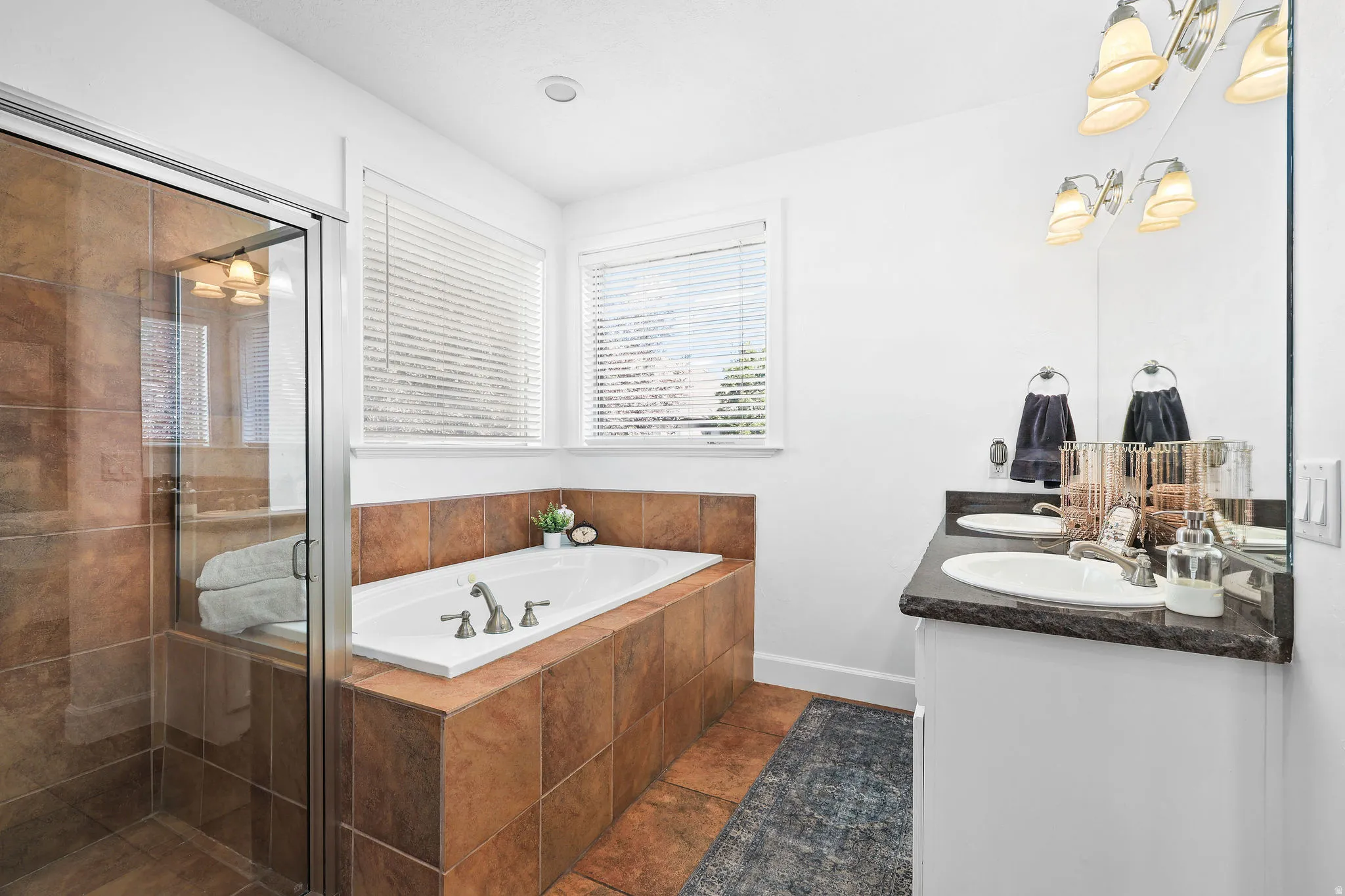 Built-in soaking tub with tile surround, glass-enclosed shower with tile walls, and a dual vanity with undermount sinks and dark countertops
