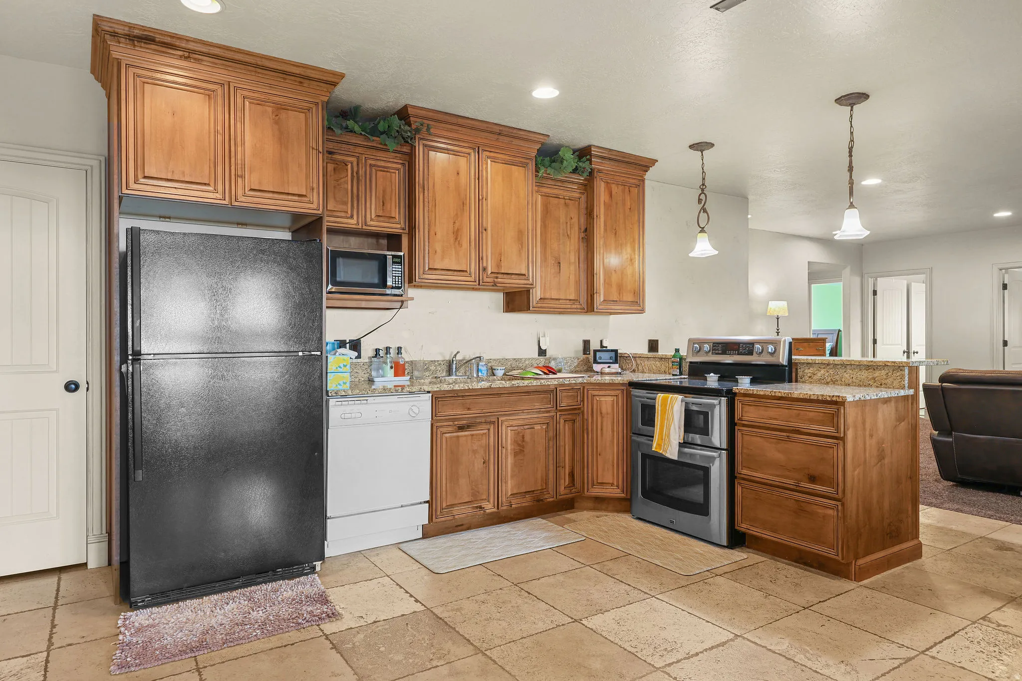 Kitchen featuring wood cabinetry, light-toned stone tile flooring, granite-style countertops, stainless steel oven, and a built-in microwave