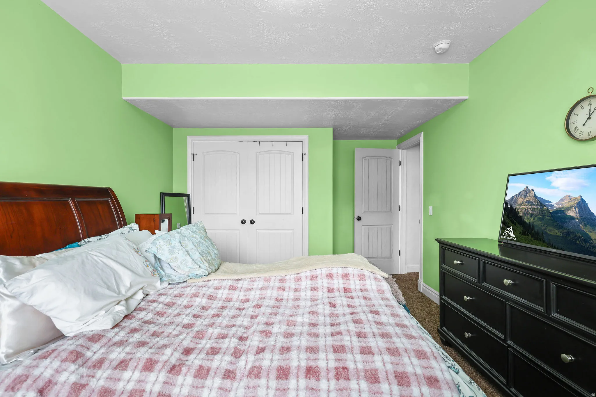 Recessed ceiling area, wood-finish headboard, white paneled double closet doors with dark hardware, white paneled door with dark hardware, and carpet flooring