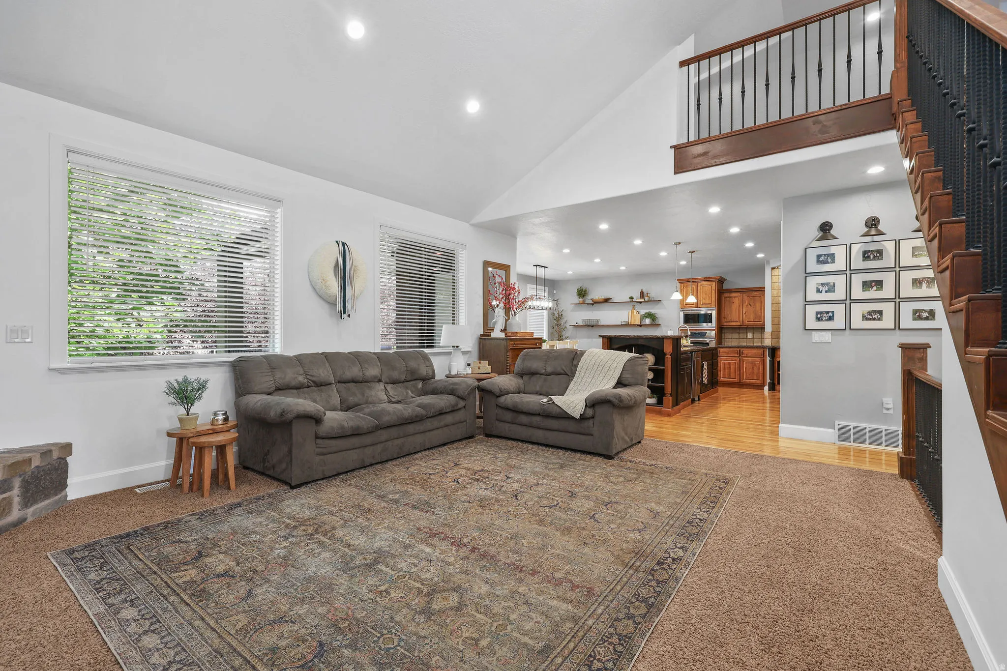 Vaulted ceiling with recessed lighting, large windows, wood-finish flooring, and a staircase with wrought iron balusters