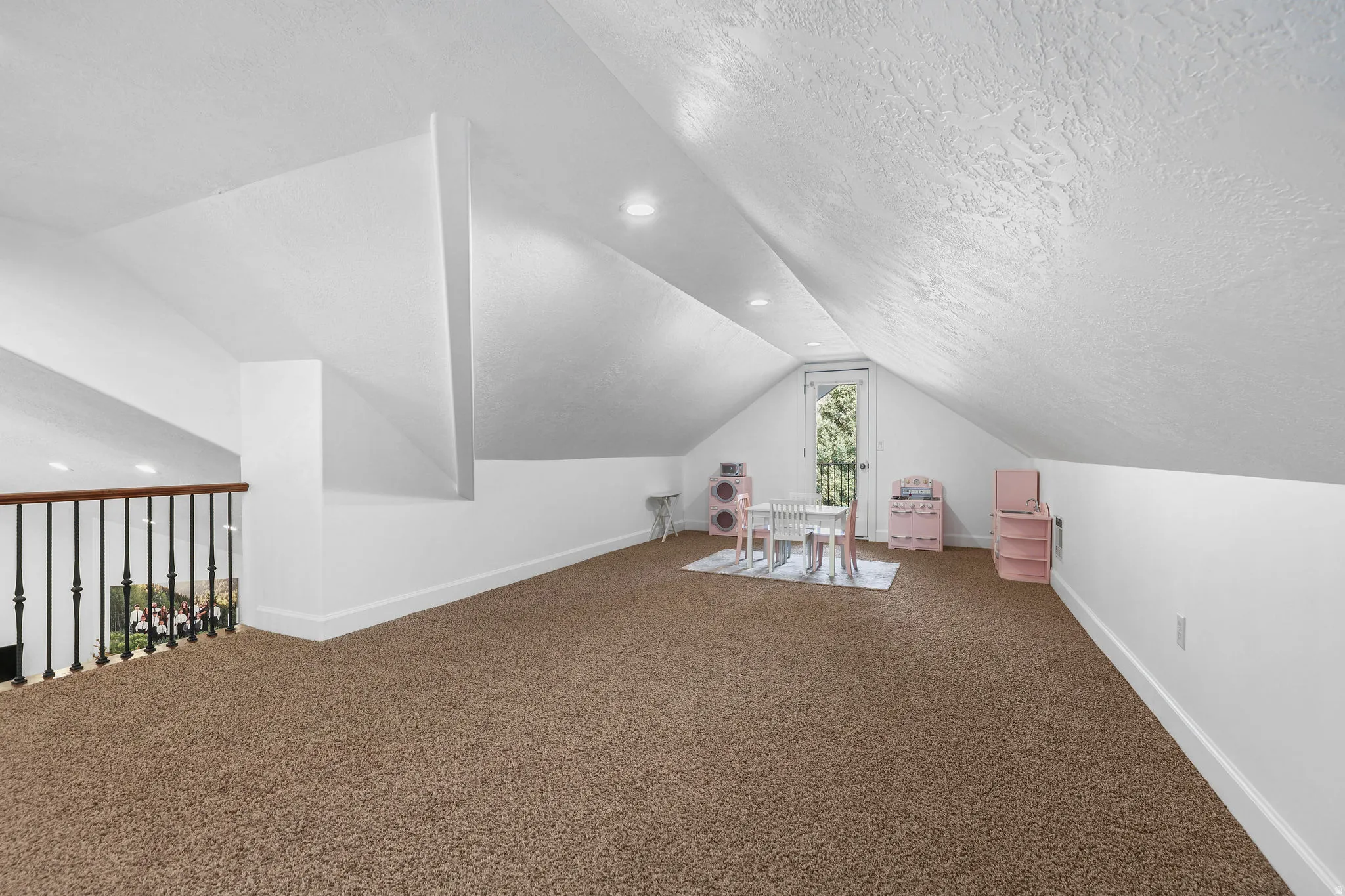 Expansive carpeted area with vaulted ceilings, recessed lighting, and a balustrade railing