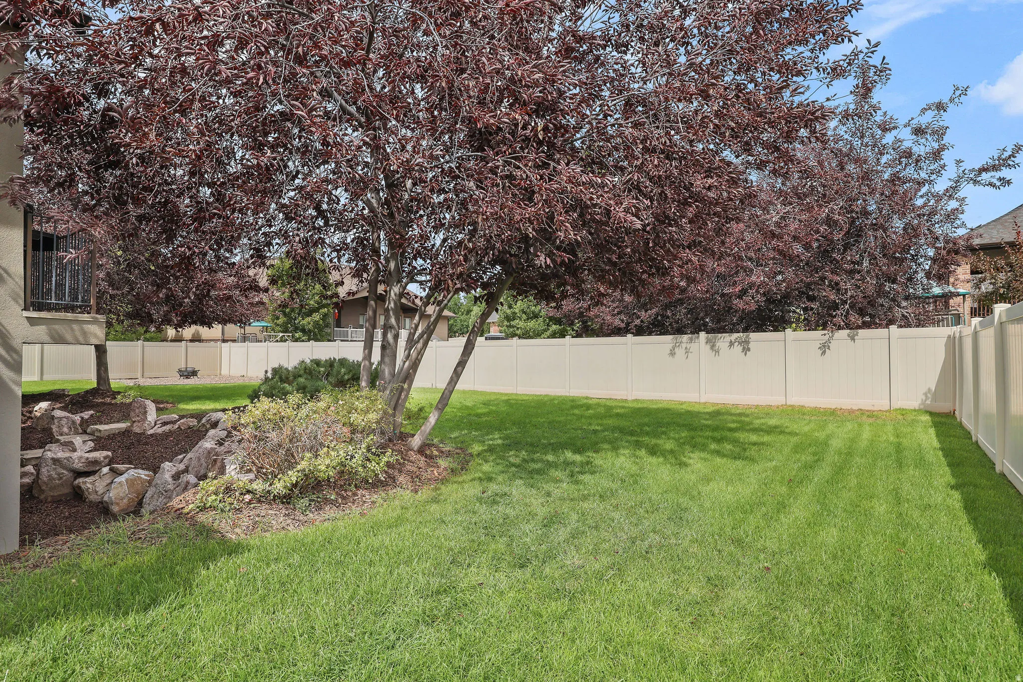 Spacious grassy yard with mature trees, a rock garden, and privacy fencing