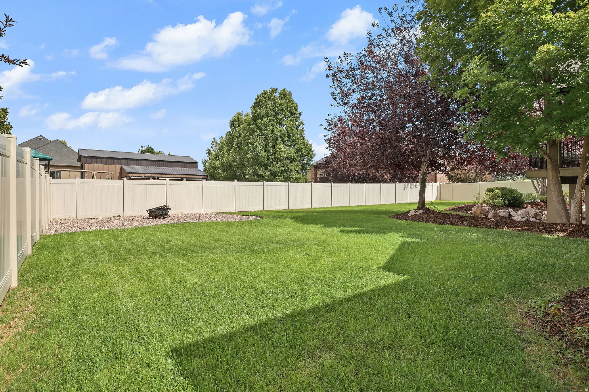 Expansive lawn with a full perimeter fence, mature trees, and a landscaped rock garden