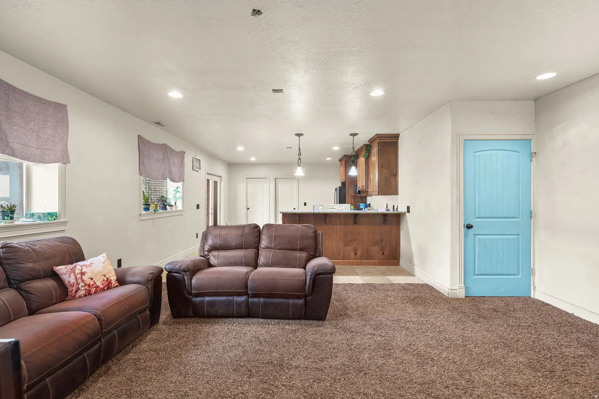 Recessed lighting illuminates the space, featuring a built-in wood-finish bar with pendant lighting and adjacent white panel doors