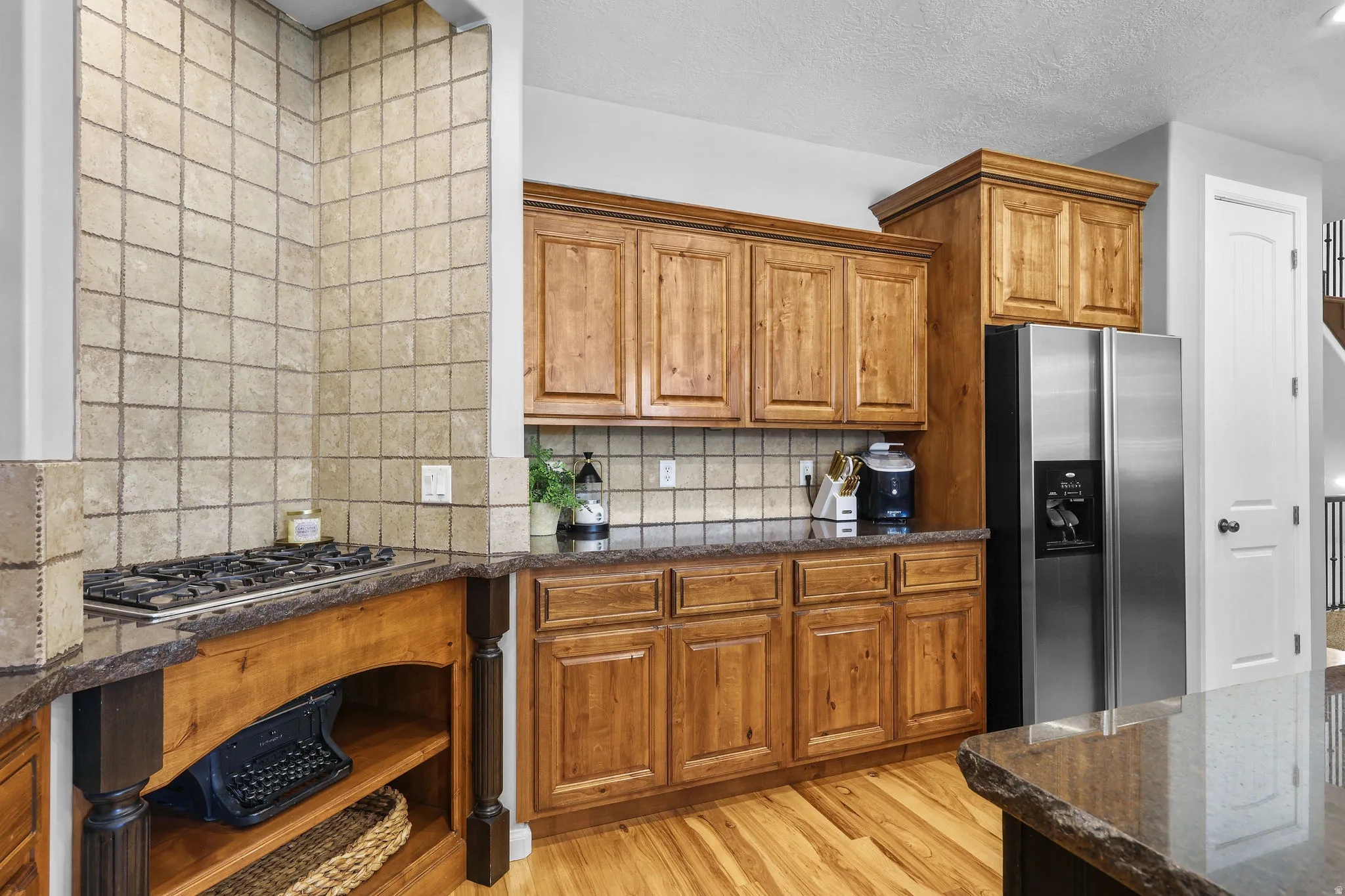 Hardwood flooring, wood-finish cabinetry, stainless steel refrigerator, gas cooktop, and stone countertops