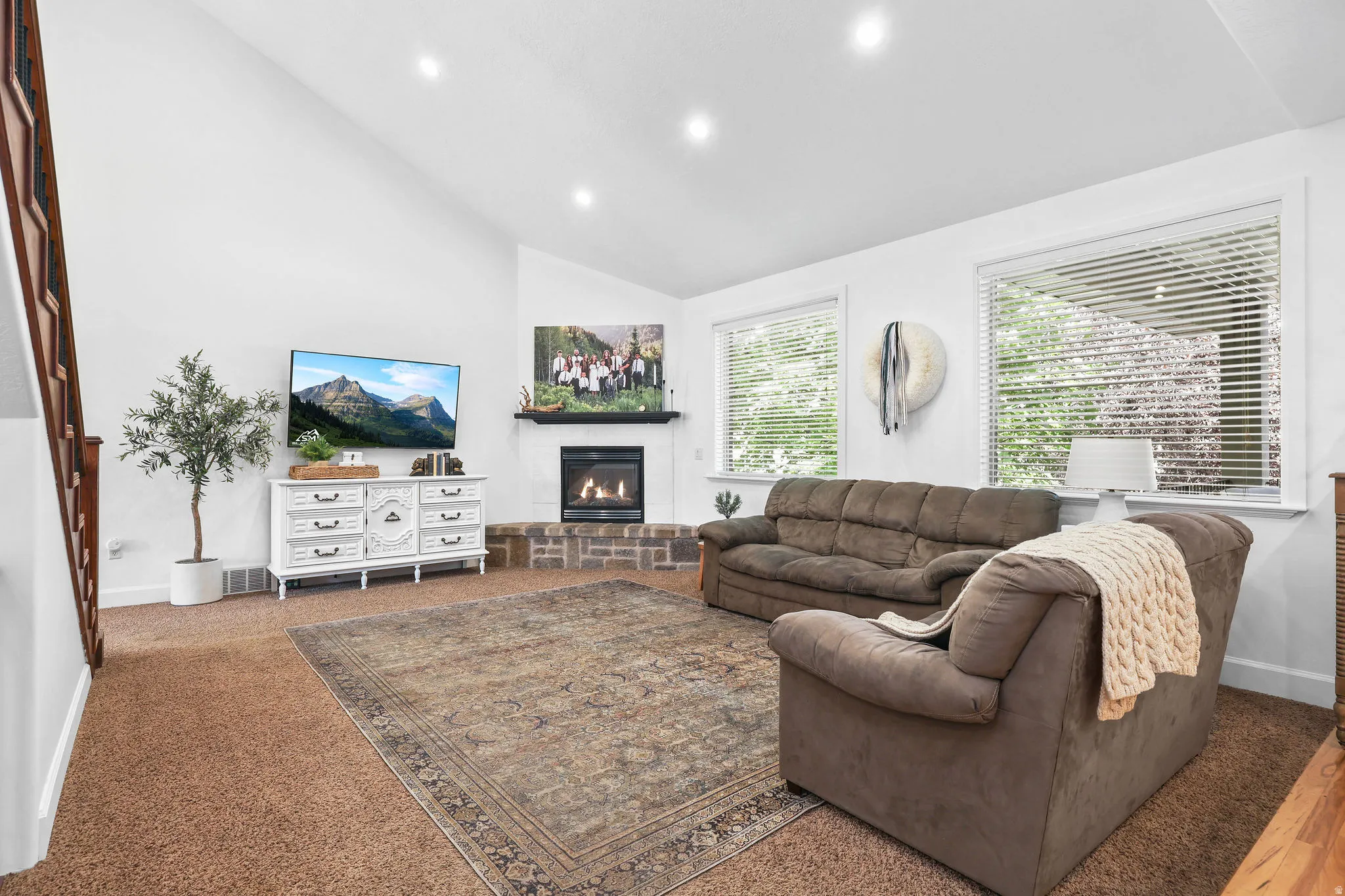 Vaulted ceiling with recessed lighting, brick-surround fireplace with mantel, and staircase with wood railing