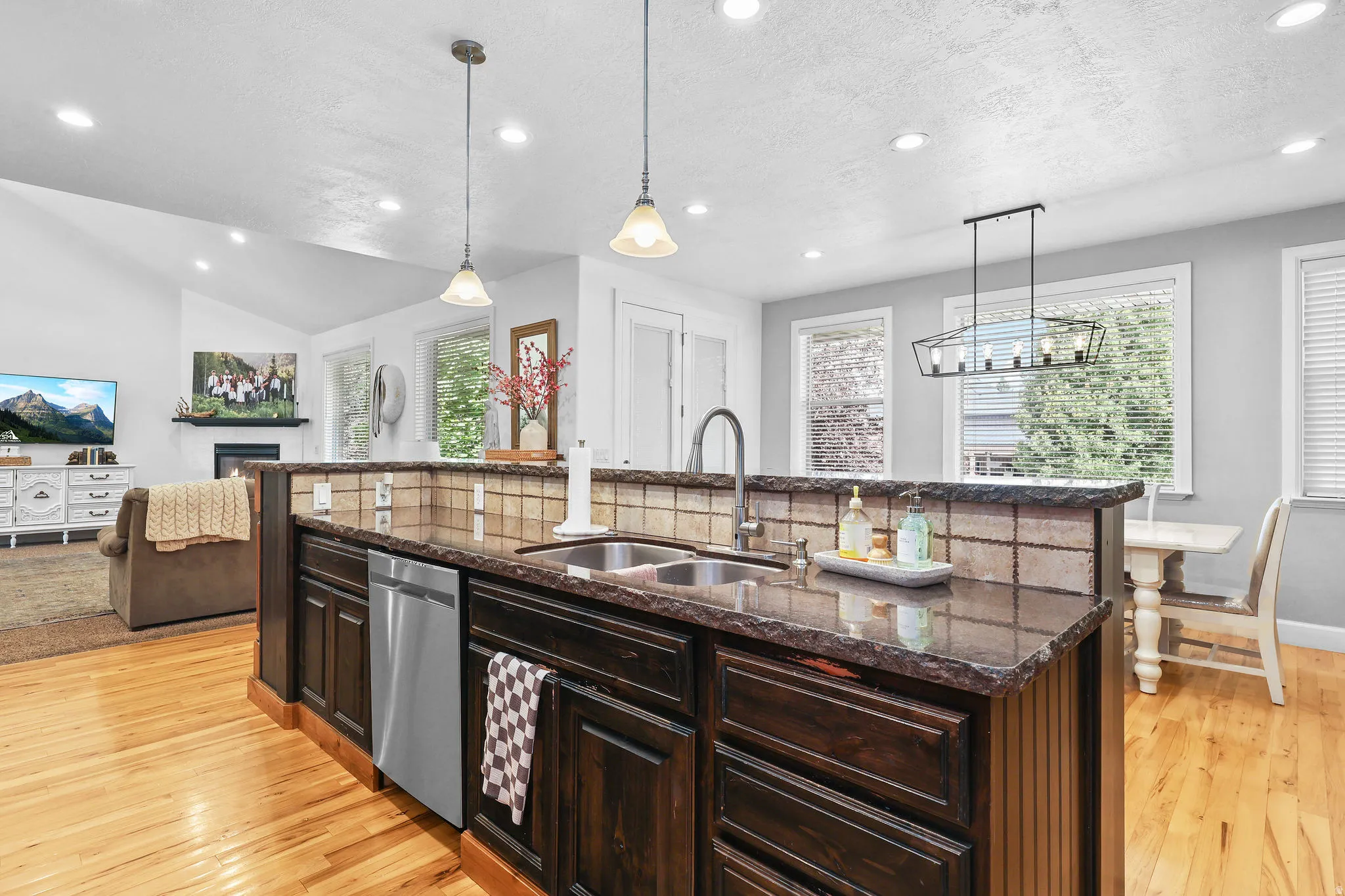 Kitchen island with dark cabinetry, integrated stainless steel dishwasher, and a dual basin sink, complemented by polished wood-finish flooring