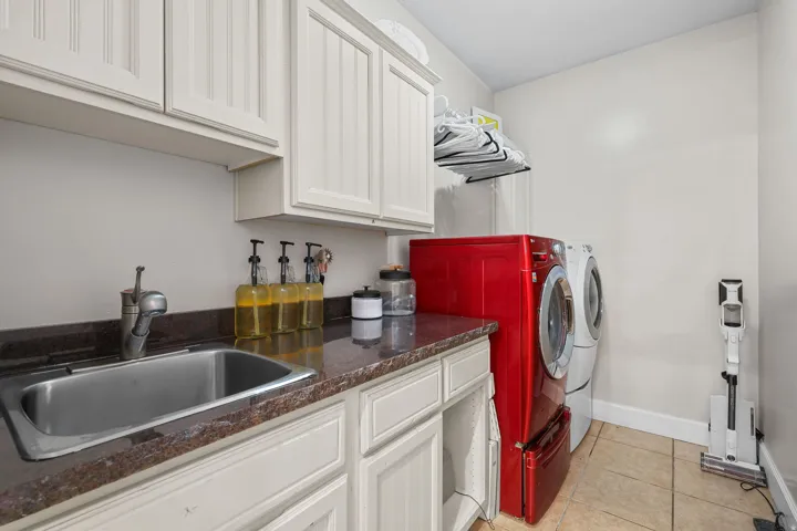 Utility room featuring white cabinetry, a stainless steel sink, a dark countertop, and tiled flooring