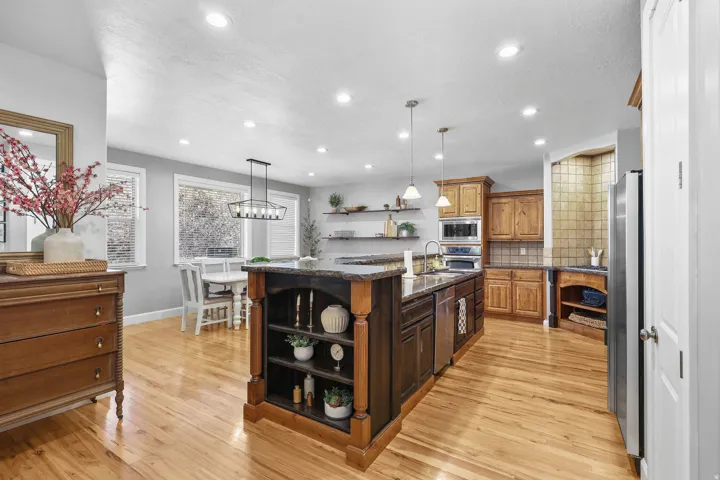 Hardwood flooring, recessed lighting, expansive kitchen island with integrated shelving, stainless steel appliances, and wood cabinetry