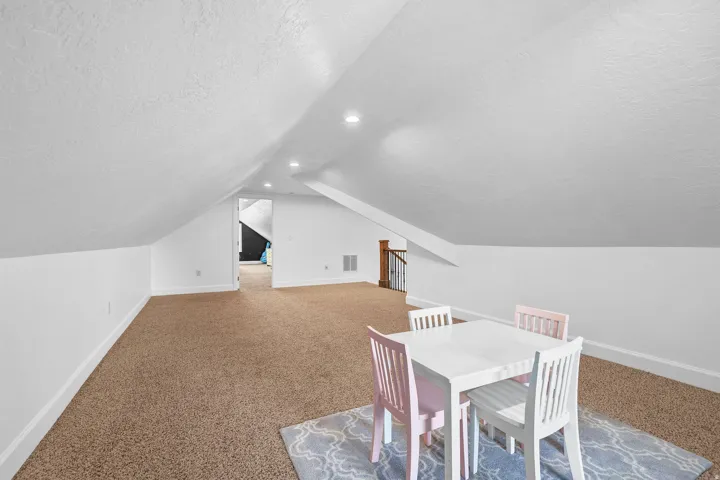 Carpeted floor, white painted walls, vaulted ceiling, recessed lighting, and a wood-finish staircase railing