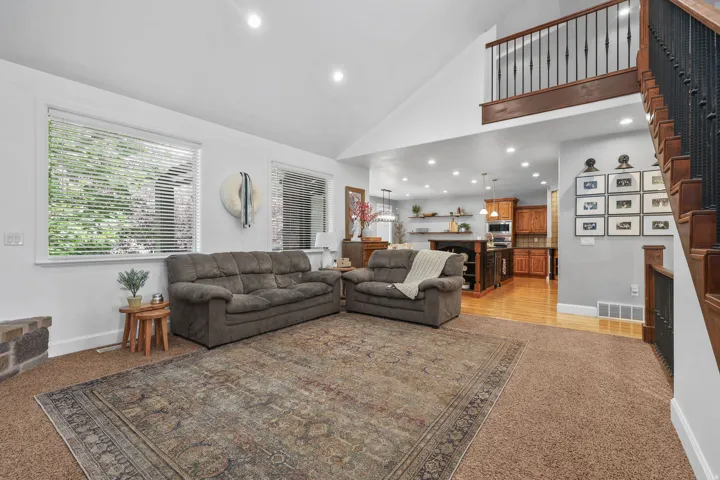 Vaulted ceiling with recessed lighting, large windows, wood-finish flooring, and a staircase with wrought iron balusters
