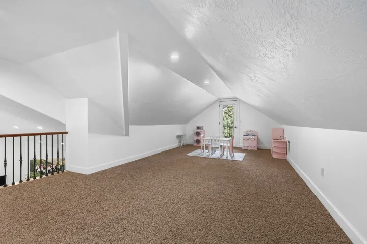 Expansive carpeted area with vaulted ceilings, recessed lighting, and a balustrade railing