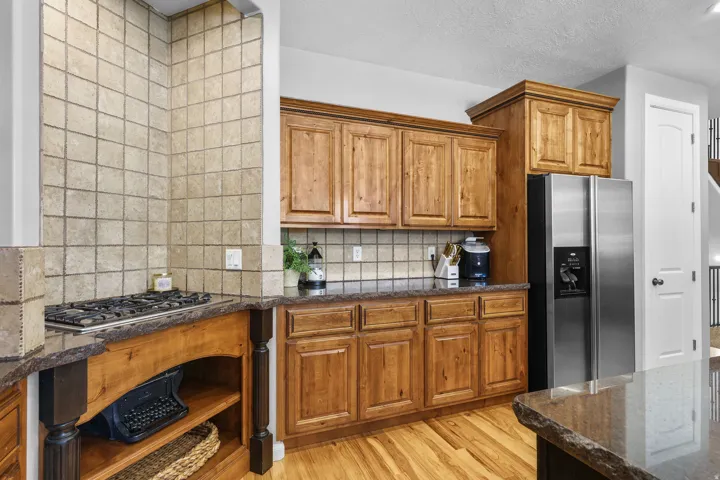 Hardwood flooring, wood-finish cabinetry, stainless steel refrigerator, gas cooktop, and stone countertops