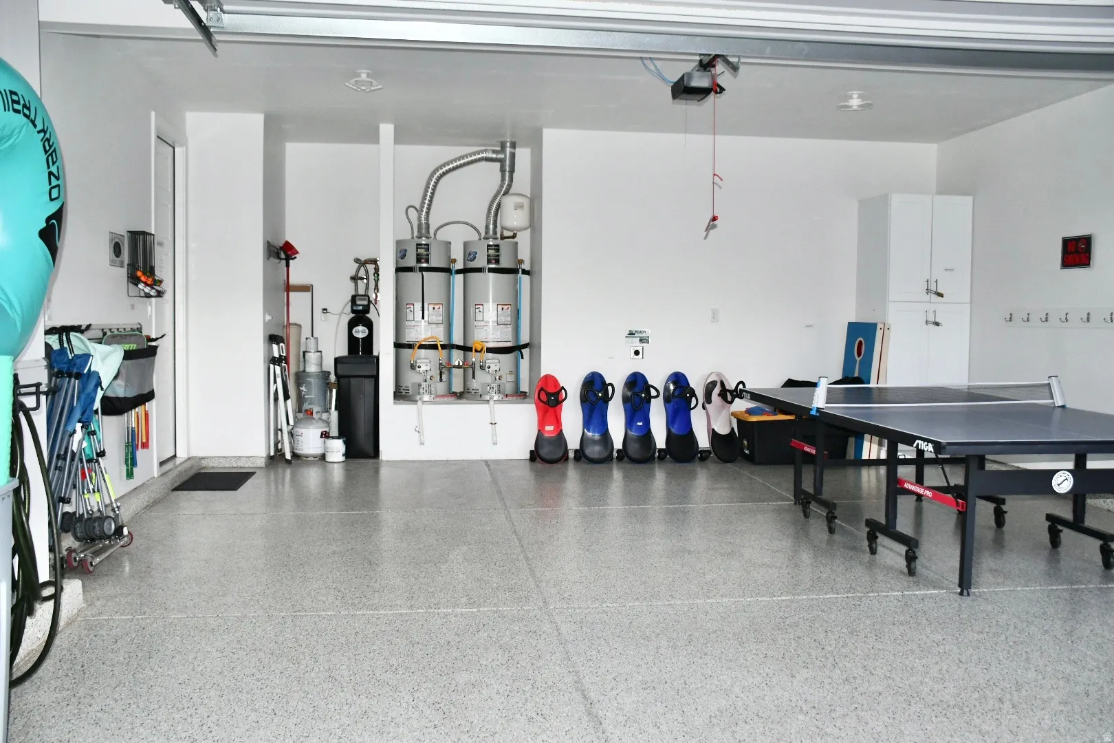 Garage space featuring a speckled epoxy floor, multiple water heaters, and built-in white cabinetry