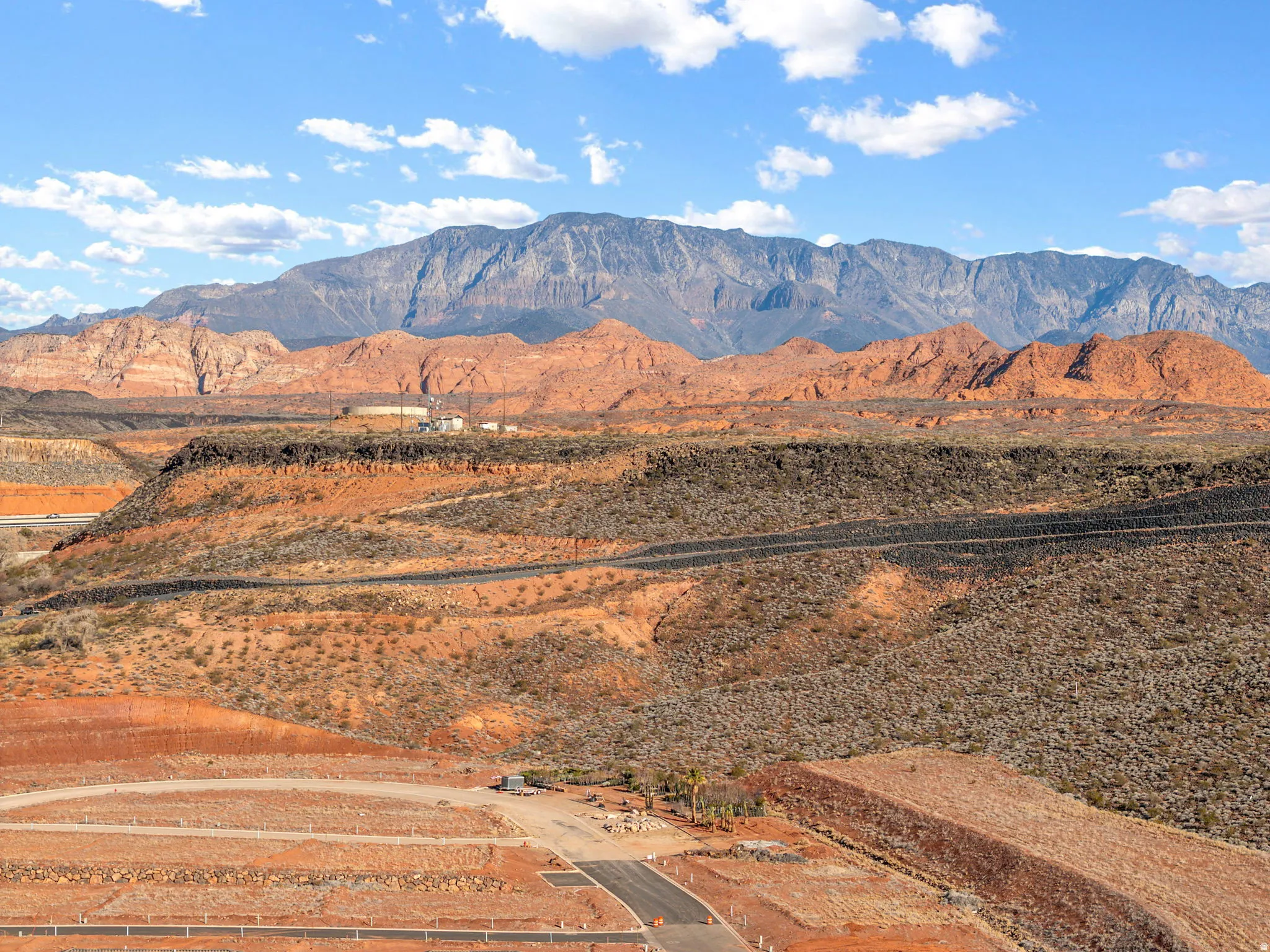 Expansive terrain featuring graded lots, paved road infrastructure, and distant mountainous backdrop