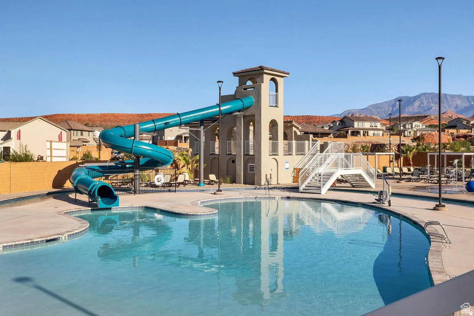 Resort-style pool area featuring a curved swimming pool, water slide, and pool deck with lounge seating