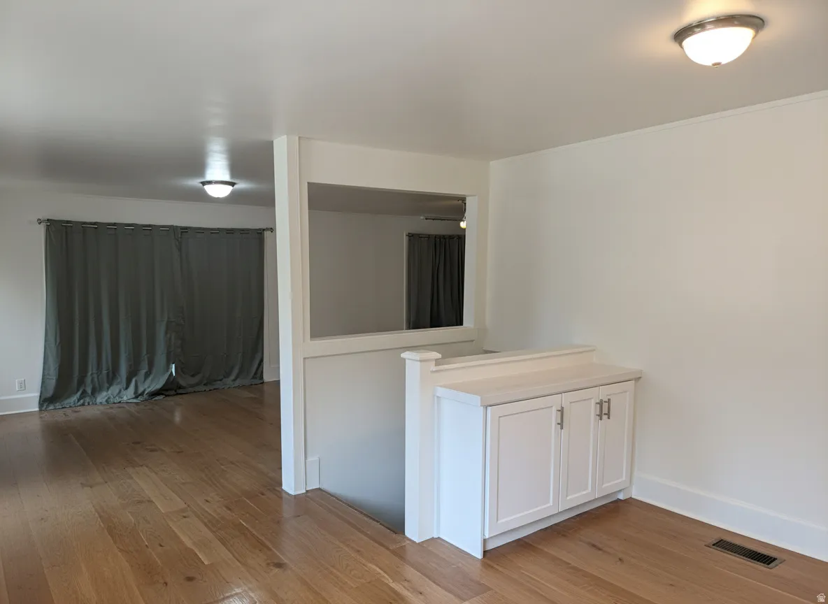 Hardwood flooring, built-in cabinetry with light-colored countertop, recessed wall opening, and flush-mount ceiling lighting