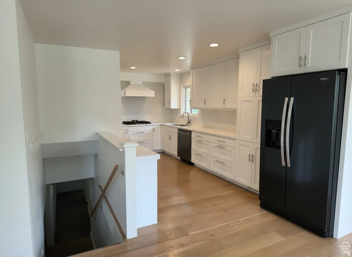 White cabinetry, light wood-finish flooring, recessed lighting, stainless steel appliances, and a built-in range hood