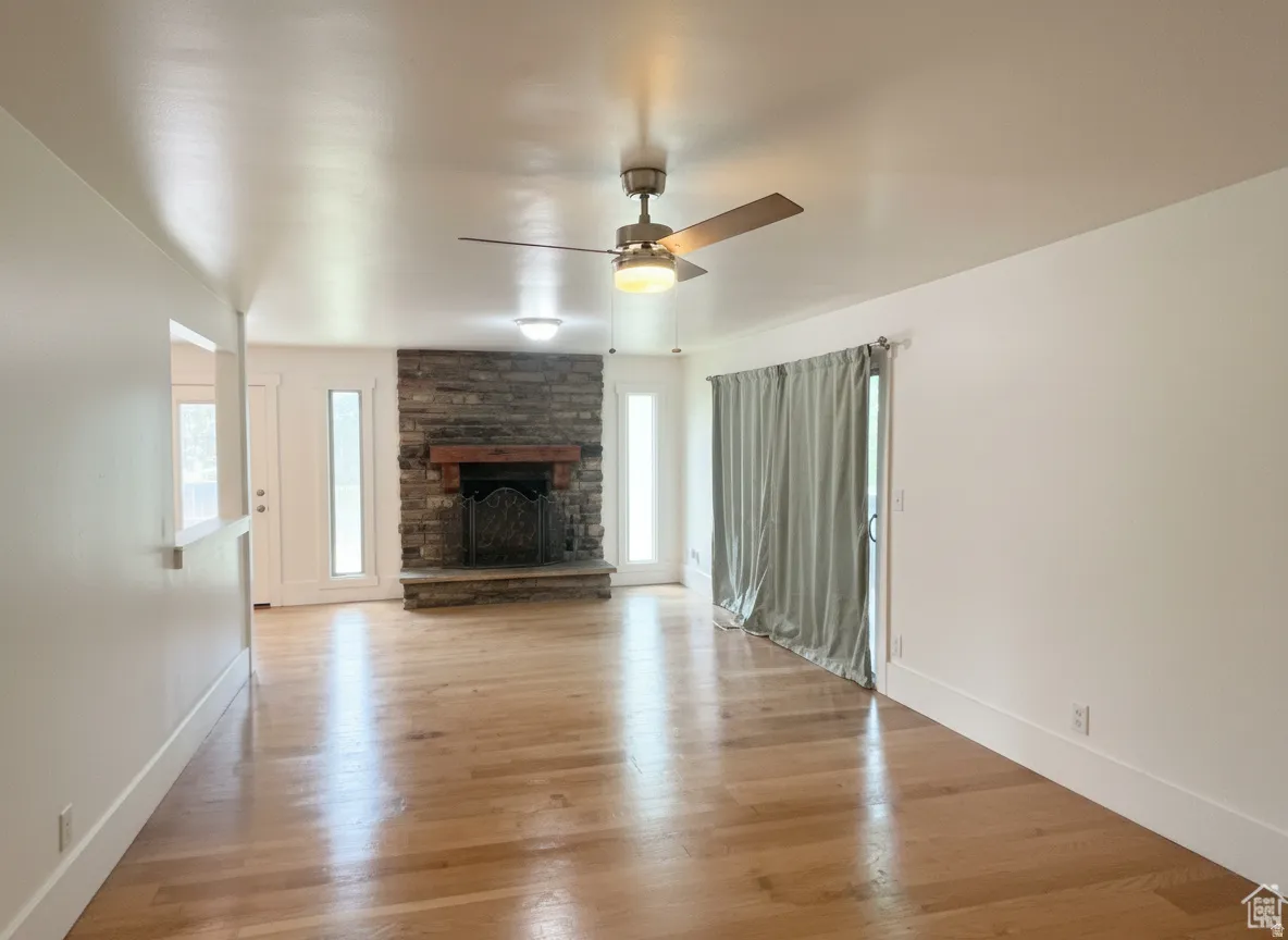 Hardwood flooring, stone-clad fireplace with wood mantel, ceiling fan, recessed lighting, and sliding glass door