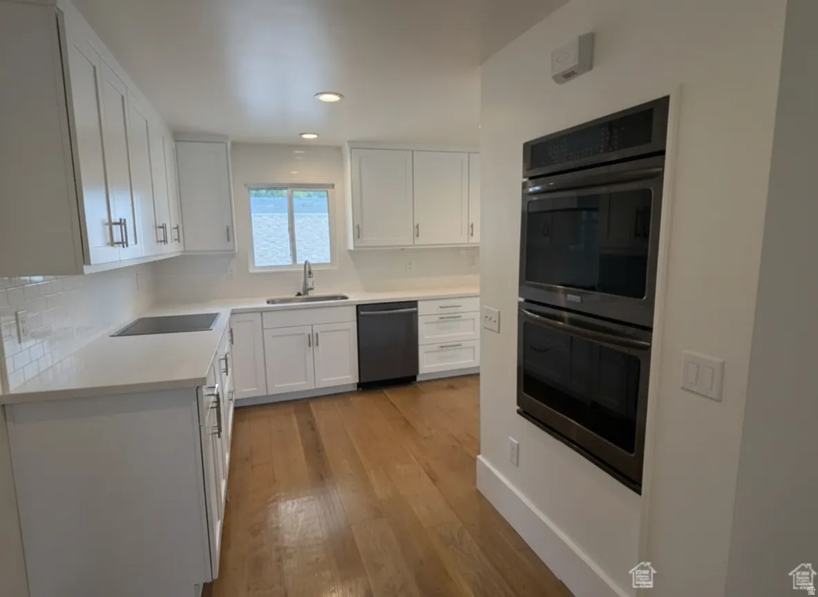 Kitchen featuring white cabinetry, light-colored countertops, stainless steel appliances, and wood-finish flooring