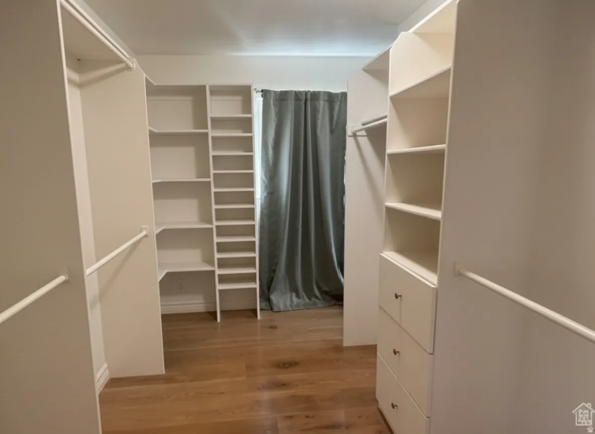 Walk-in closet featuring wood-finish flooring, built-in shelving, integrated drawers, and hanging rods