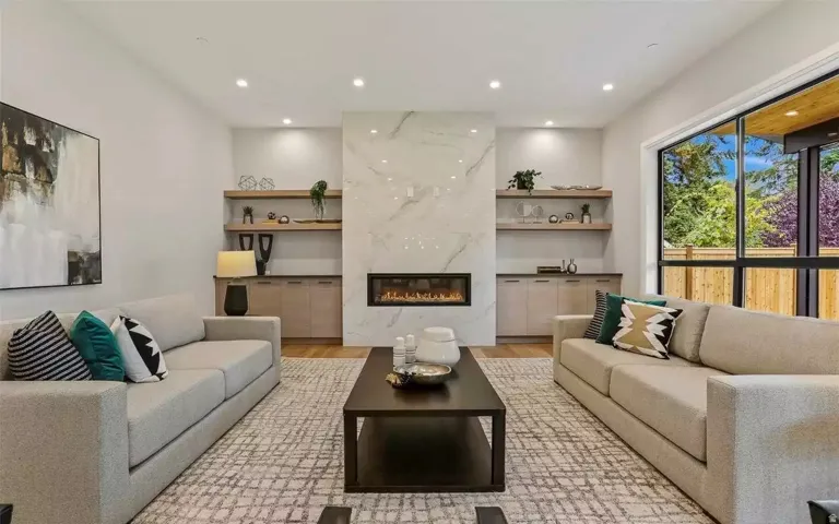 Spacious living area featuring a floor-to-ceiling marble-look fireplace with an integrated linear firebox, custom built-in cabinetry, floating wood-finish shelving, recessed lighting, and large picture windows