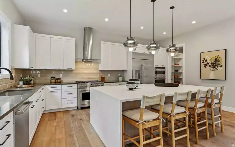 Modern kitchen featuring a large central island, overhead pendant lighting, stainless steel appliances, and wood-finish flooring