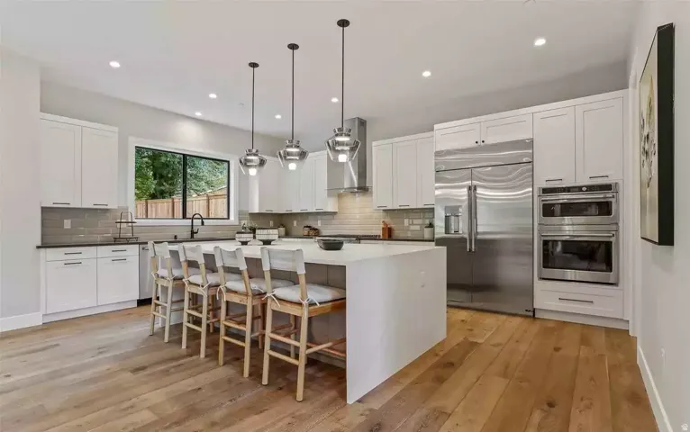 Gourmet kitchen featuring a large central island, stainless steel appliances, abundant white cabinetry, light wood-finish flooring, and recessed lighting