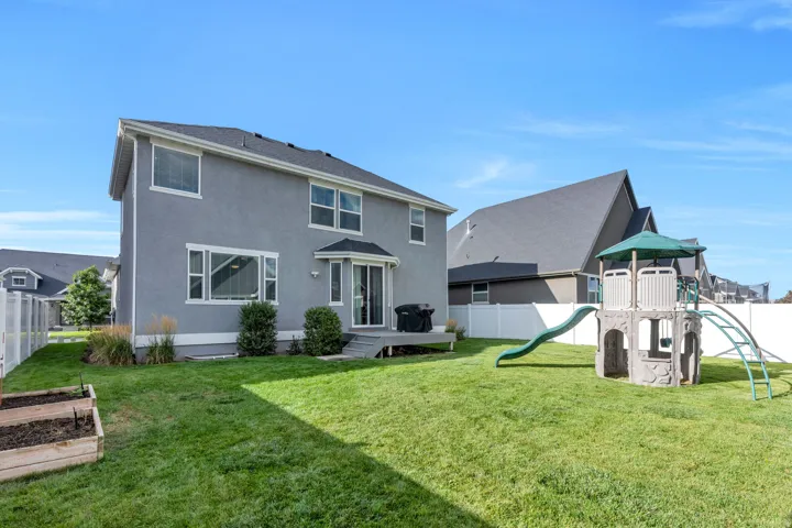 Expansive backyard featuring a manicured lawn, white vinyl fencing, and raised garden beds