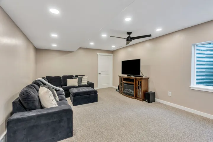 Carpeted living space featuring recessed lighting, a ceiling fan, and a white window with a well guard