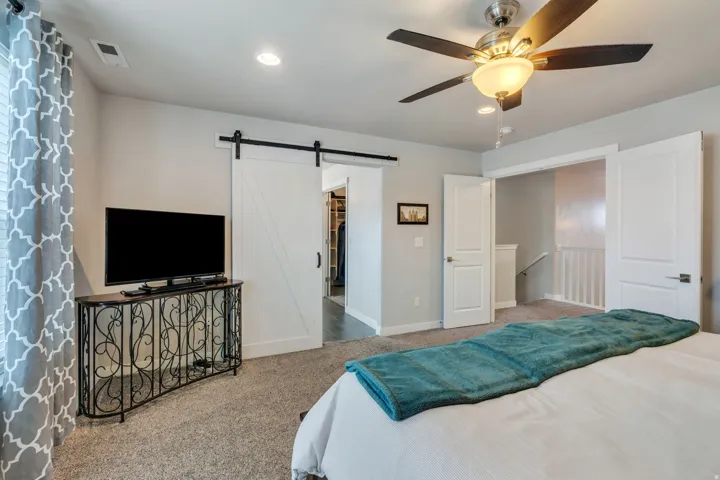 Carpeted flooring throughout, recessed ceiling lighting, a ceiling fan with integrated lighting, a white barn door, and a partially visible walk-in closet
