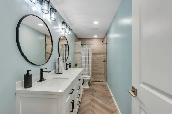 Dual vanity with white cabinetry, matte black hardware, and round mirrors