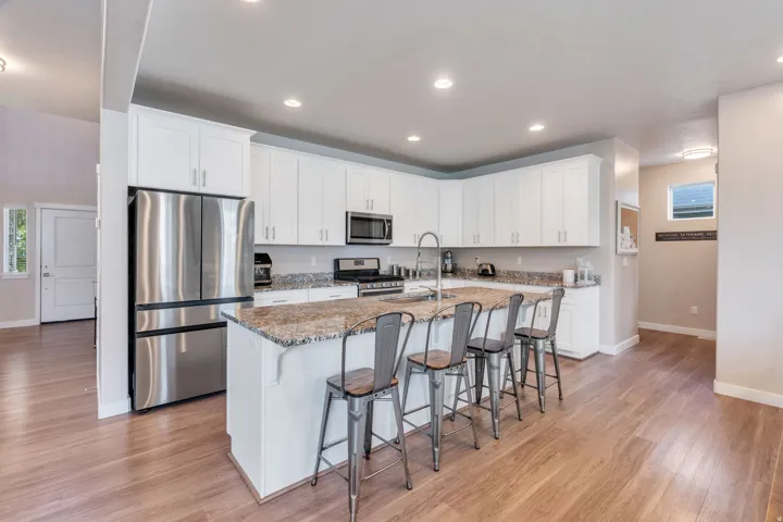 Kitchen featuring white cabinetry, stainless steel appliances, a center island with seating, stone countertops, and wood-finish flooring