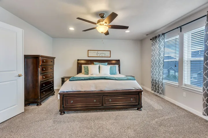 Carpeted bedroom featuring two windows with blinds, recessed lighting, and a ceiling fan with integrated light