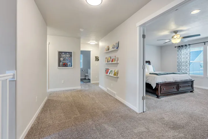 Carpeted hallway with painted walls, recessed lighting, and a doorway leading to a room with a ceiling fan