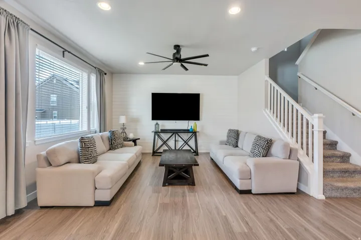 Open-concept living area featuring wood-finish flooring, a ceiling fan with integrated lighting, recessed ceiling lights, and a built-in media console